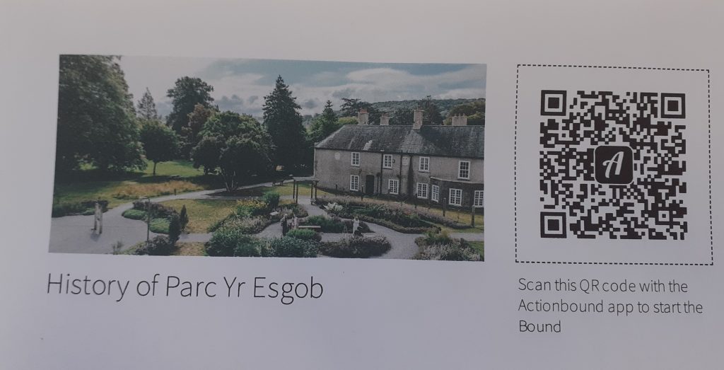  Mae tŷ carreg mawr gyda simneiau lluosog yn eistedd ymhlith coed a gerddi; wrth ei ymyl mae cod QR a thestun yn darllen Hanes Parc Yr Esgob. Sganiwch y cod QR hwn gyda'r ap Actionbound i gychwyn y Bound. 